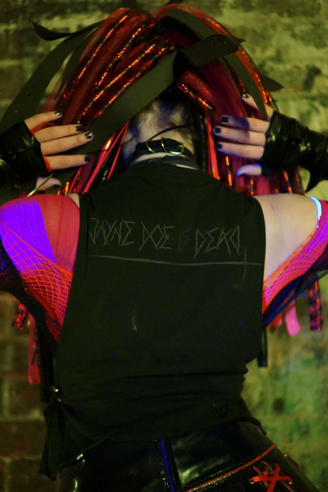 Cybergoth in post apocalyptic scene wearing red cyber falls and a black tank top with a black jayne doe is dead logo printed on the back in black goth style font