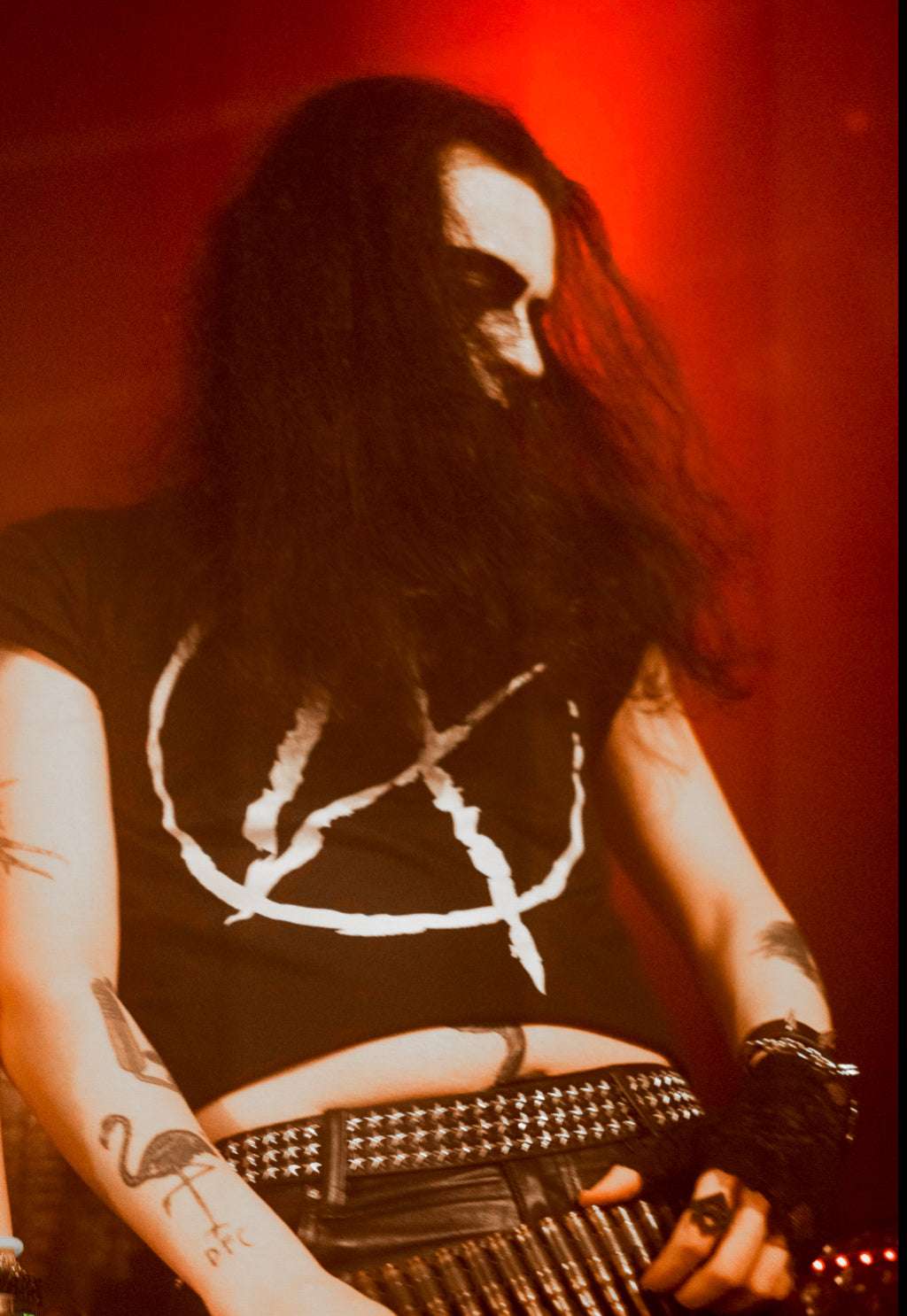 Goth guy with long hair wearing a black cropped tshirt with a big white A (for anarchy) print on the front