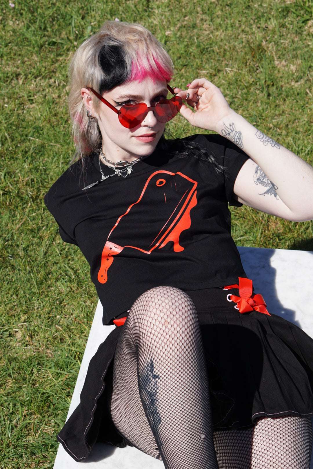 Off with their Heads Cropped Tee in black featuring bold red cleaver graphic, styled with fishnet tights and pleated skirt for alt streetwear look.
