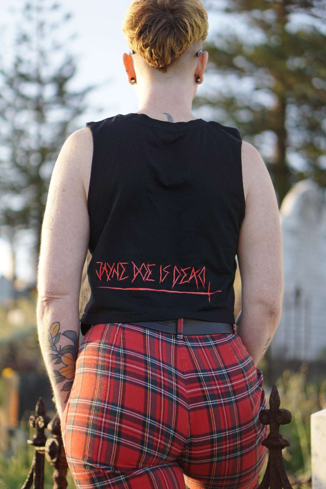 Back view of Off with their Heads Cropped Tank showing 'Jayne Doe is Dead' text in red gothic font, styled with red plaid pants.