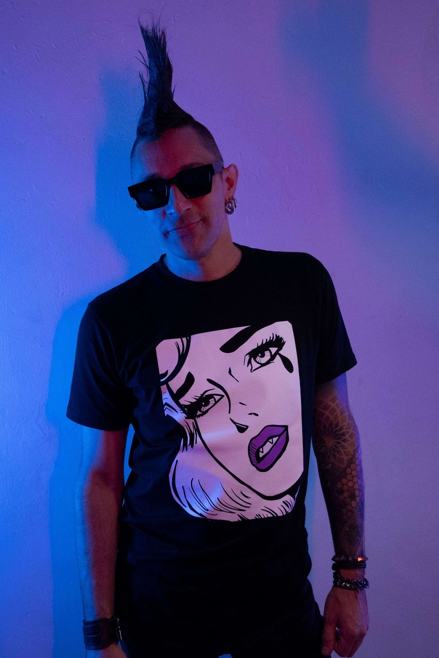 Tall guy with huge black mohawk wearing a black long tshirt with an extra large white pop art woman's face crying one tear with fangs & purple lips.
