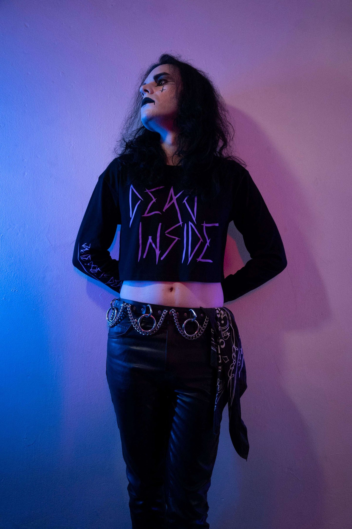 Goth boy wearing a long sleevblack cropped tshirt with the words dead inside printed on the front in purple gothic font. The arm has a jayne doe is dead