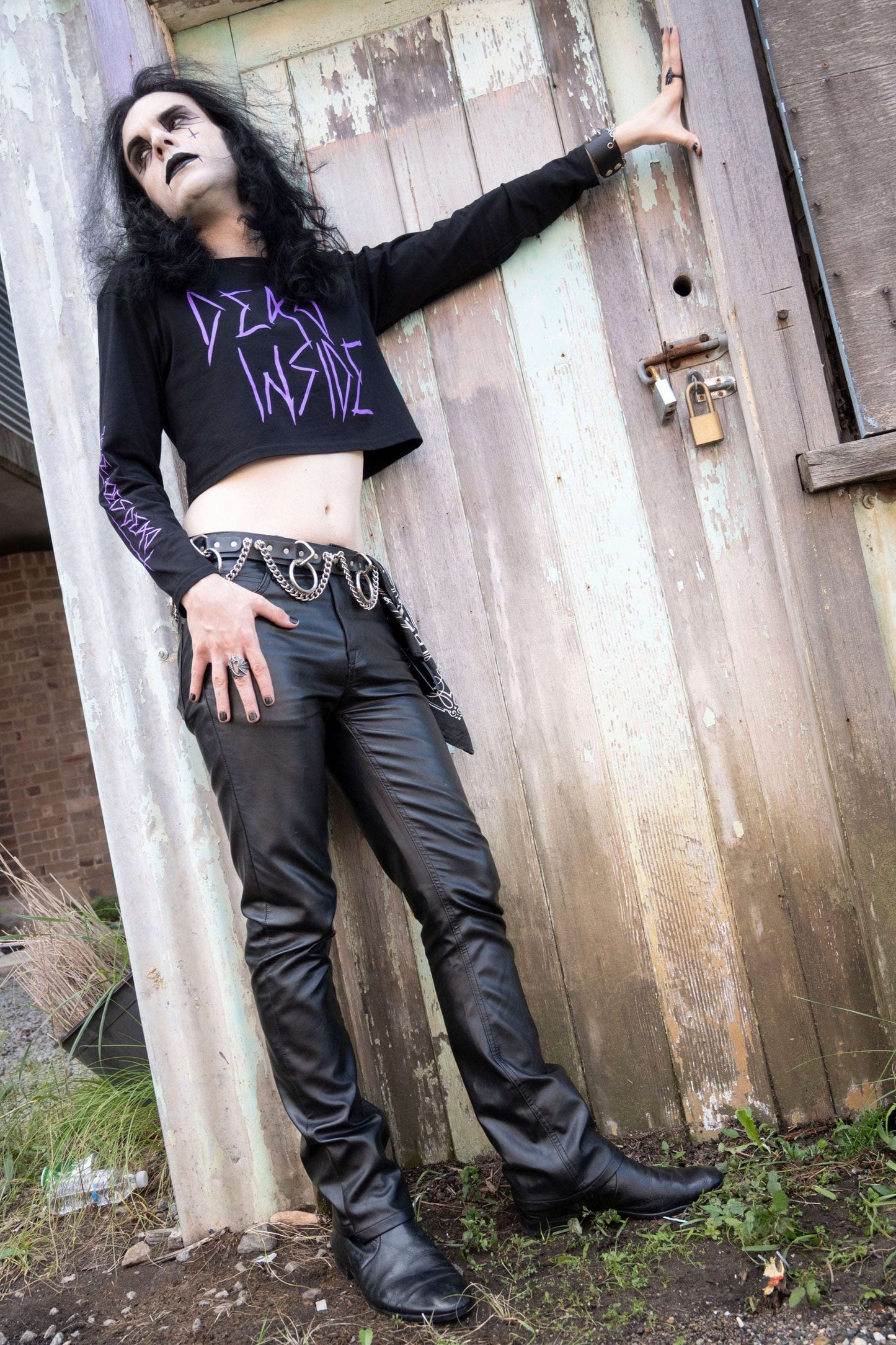 Goth boy wearing a long sleeve black cropped tshirt with the words dead inside printed on the front in purple gothic font. The arm has a jayne doe is dead