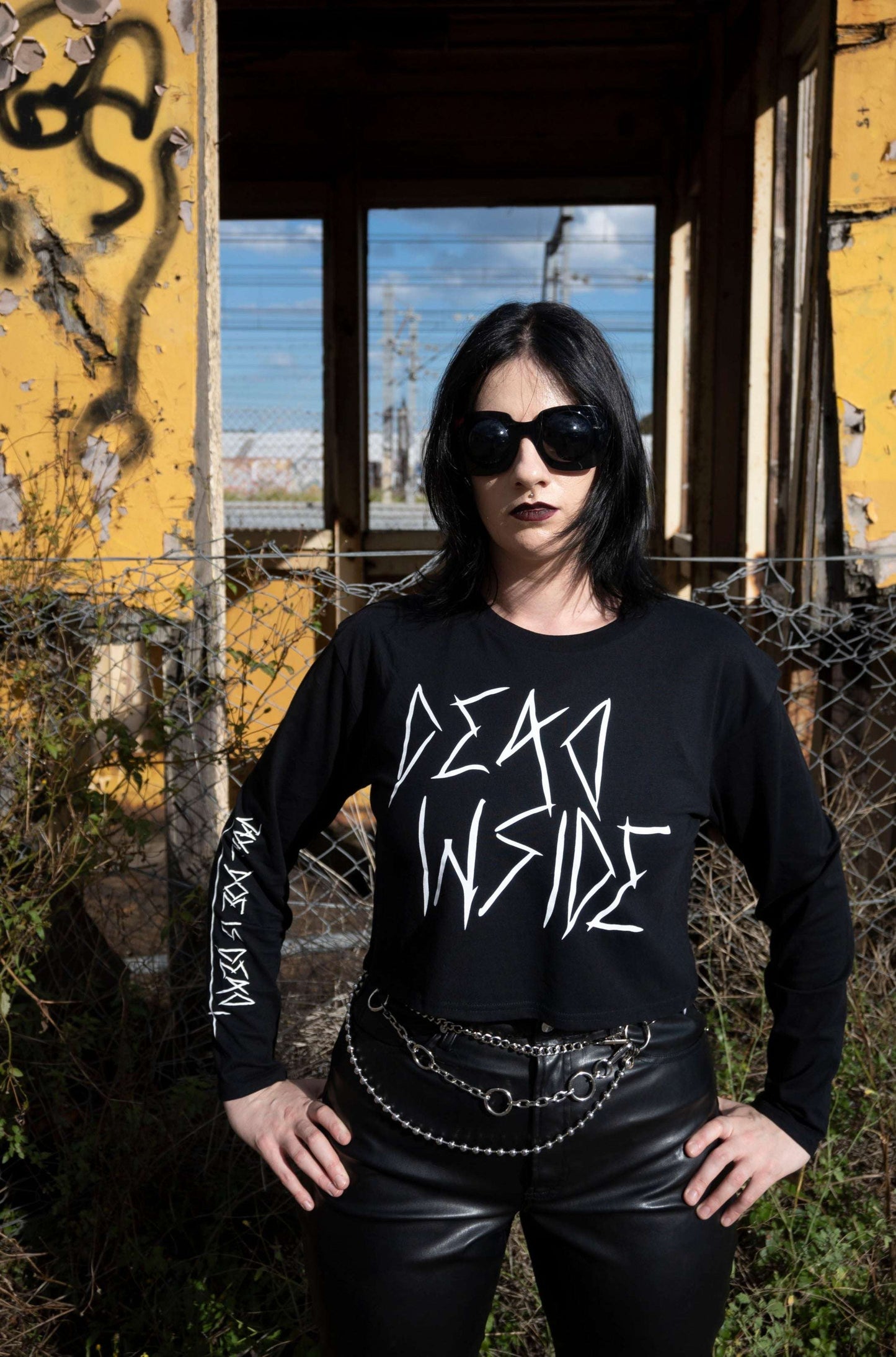 Goth girl wearing a long sleeve black cropped tshirt with the words dead inside printed on the front in white gothic font. The arm has a jayne doe is dead logo
