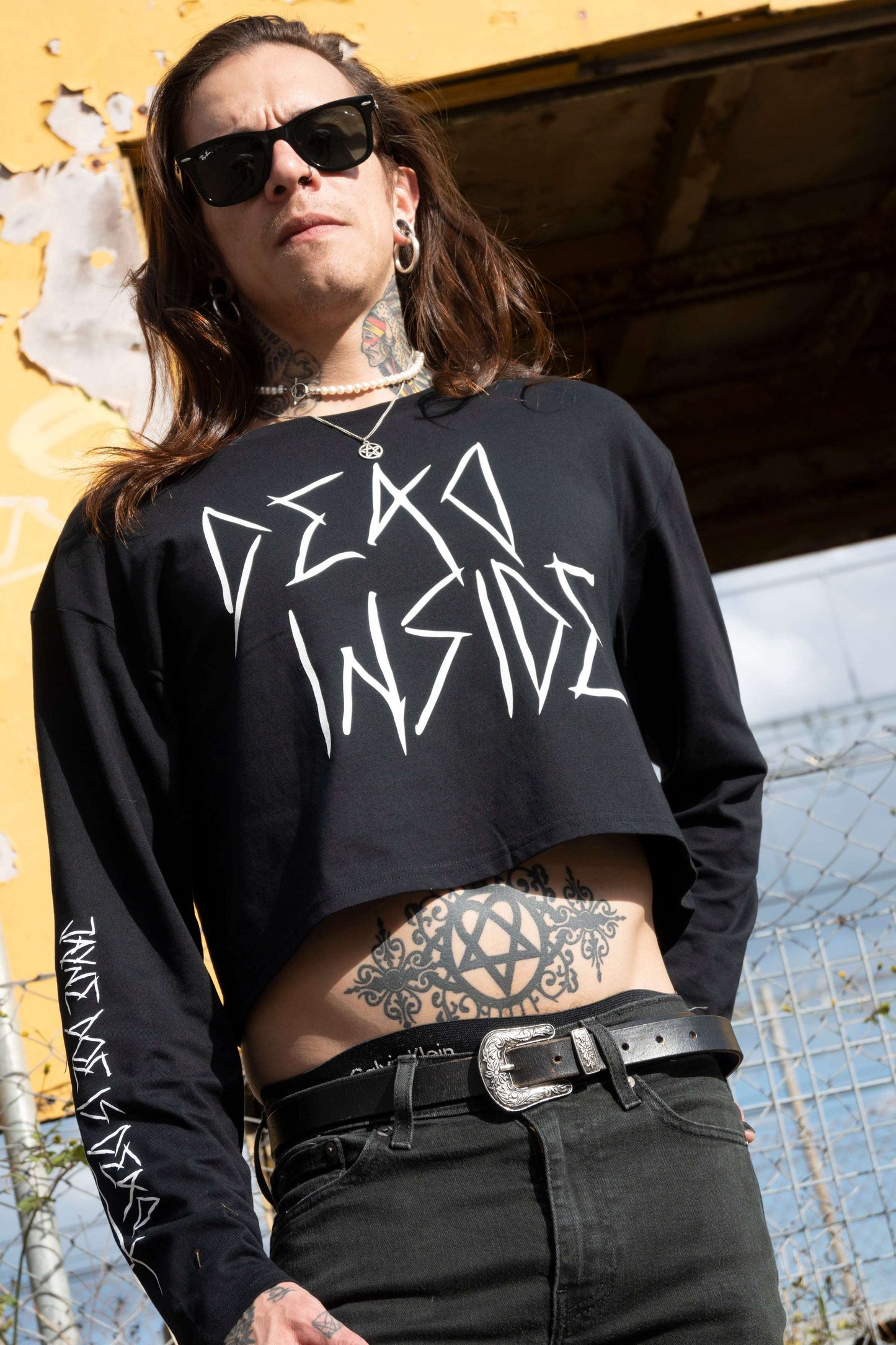 Alt boy wearing a long sleeve black cropped tshirt with the words dead inside printed on the front in white gothic font. The arm has a jayne doe is dead