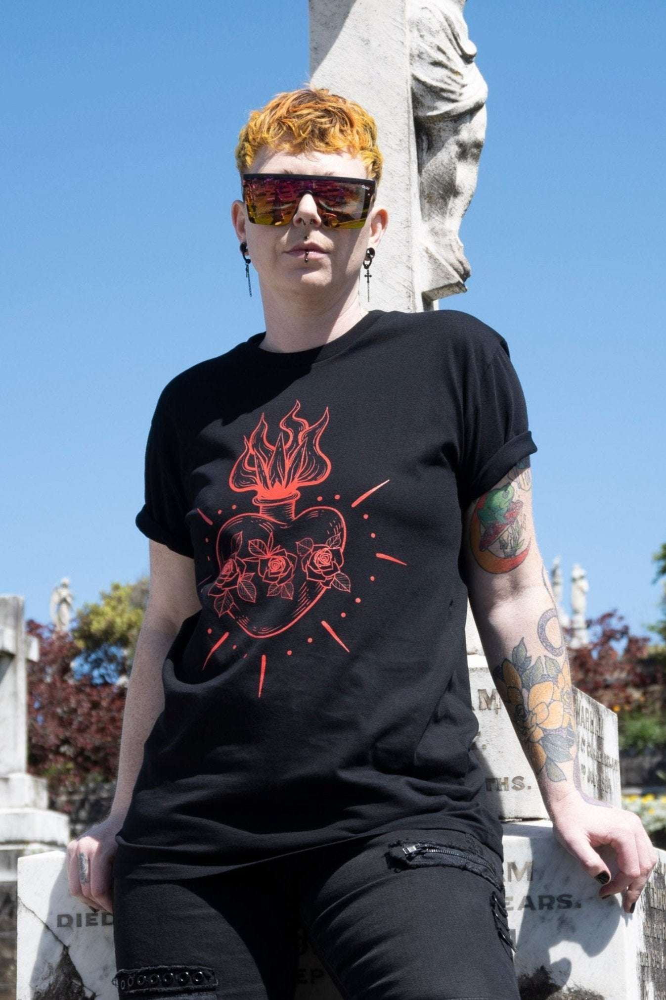 Queen of Hearts Tee in black featuring red sacred heart graphic with roses and flames, styled with rolled sleeves for alt streetwear look.