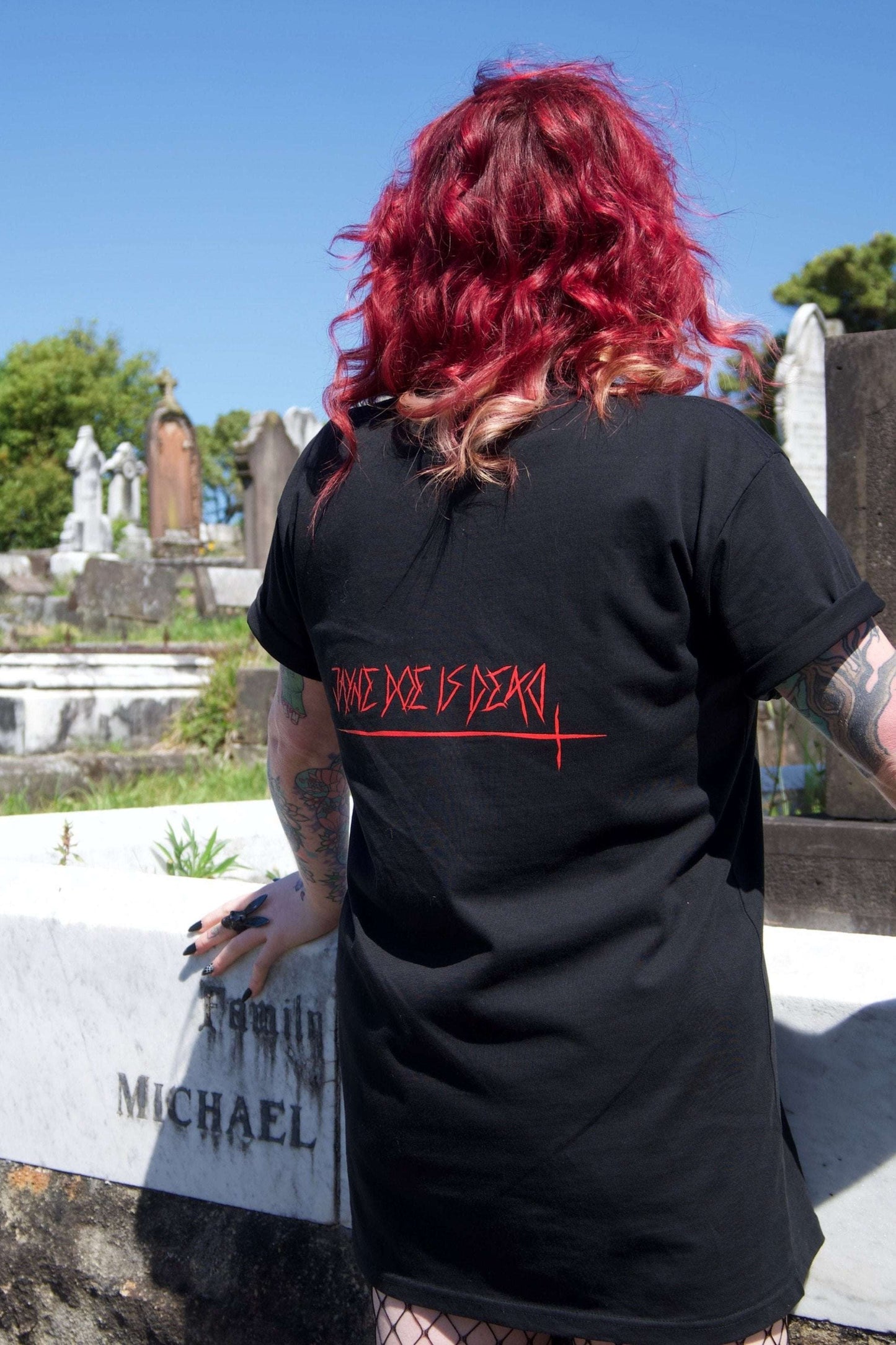 Off With Their Heads Xtra Long Tee / Dress in black with red 'Jayne Doe Is Dead' text on back, worn by model in cemetery setting. Gothic streetwear style.