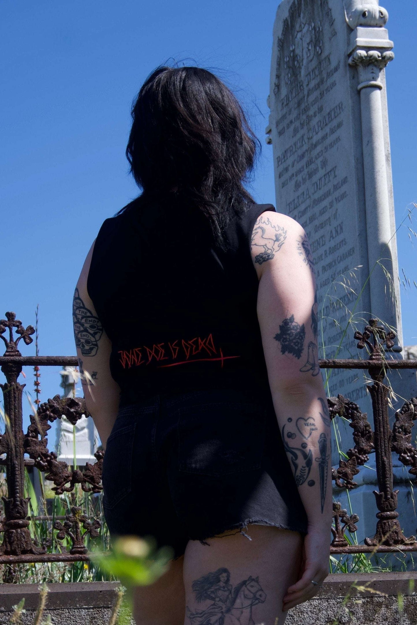 Back of Off with their Heads Cropped Tank displaying red gothic text, paired with black shorts in a punk-inspired cemetery shoot.