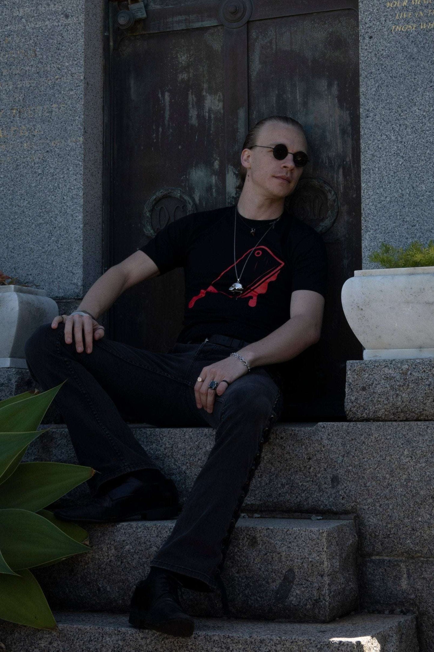 Model wearing Off with their Heads Tee seated on stone steps, showcasing the graphic cleaver design for alternative and emo fashion styling.