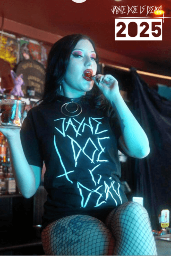2025 Wall Calendar featuring gothic alternative model in fishnet tights and Jayne Doe Is Dead t-shirt, holding a drink and cherry in a bar setting.