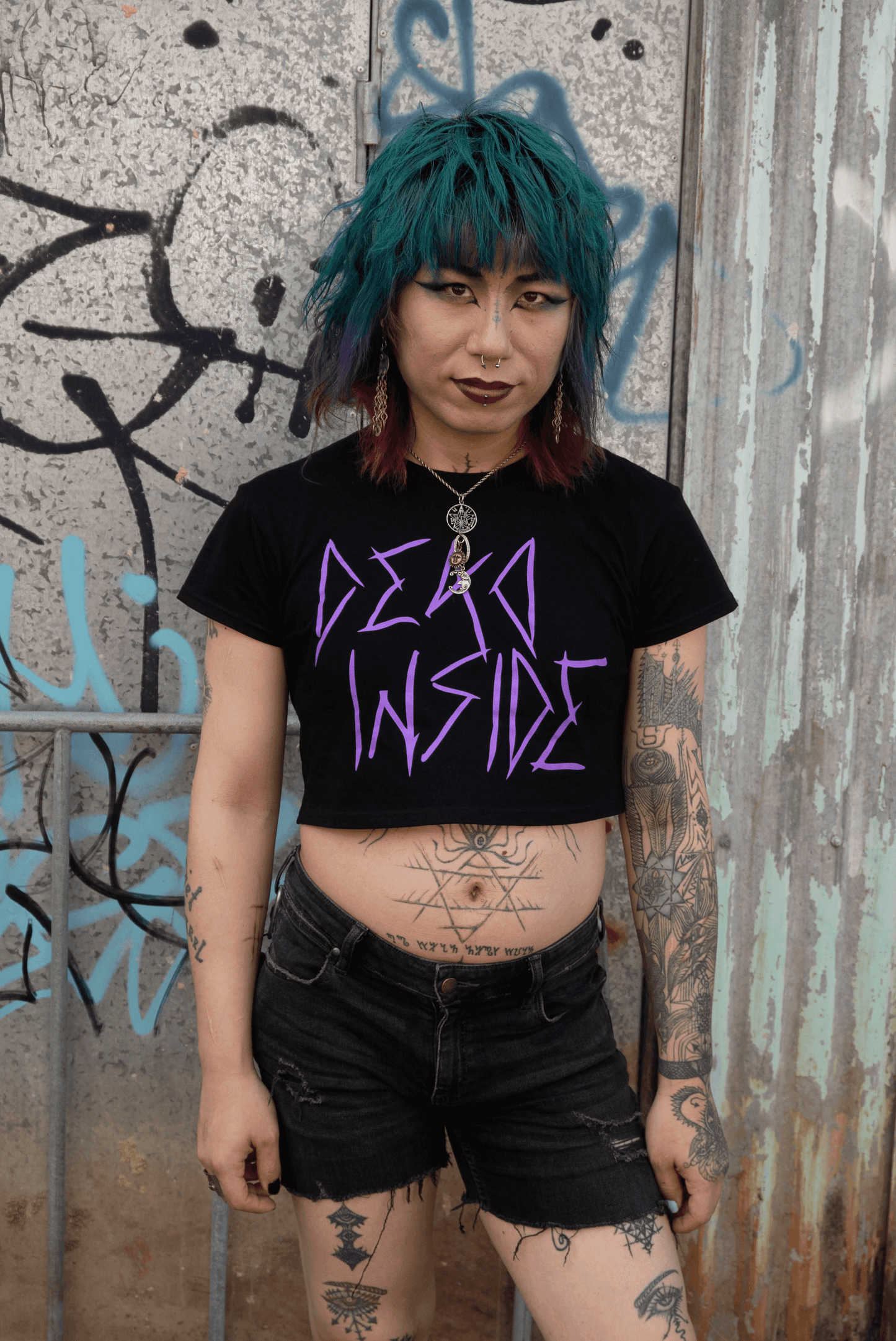 Goth trans girl wearing a black cropped Tshirt with dead inside printed on the front in purple gothic style font