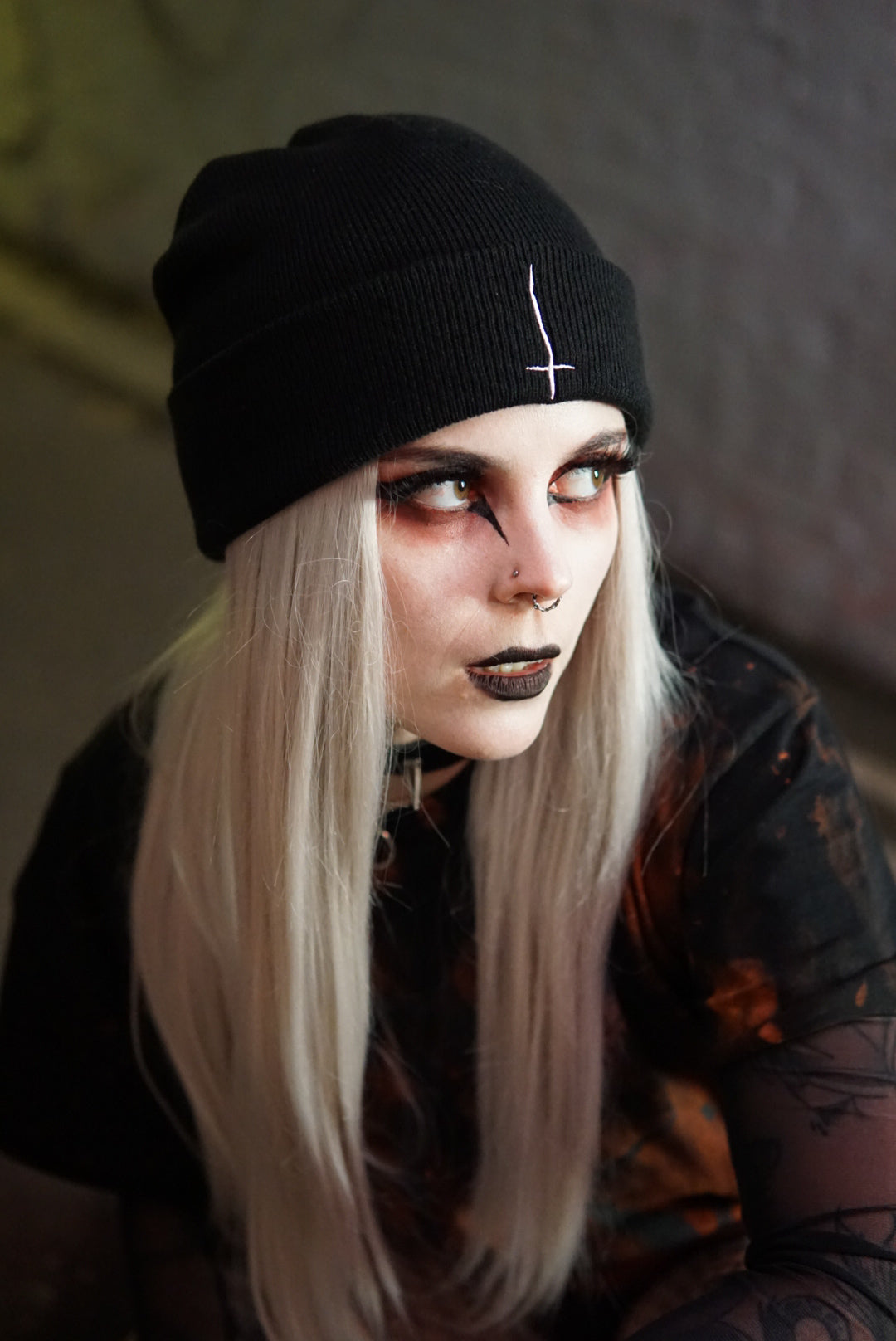 Sinner Beanie in black with white inverted cross embroidery, worn by model with gothic makeup and bleached hair. Tight knit, relaxed fit hat.