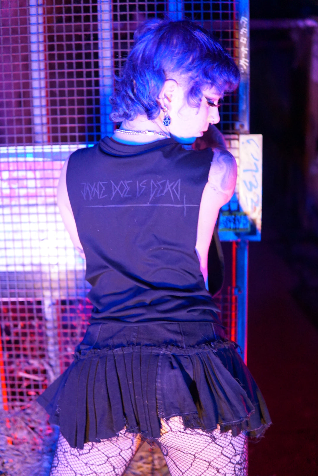 Back view of a non binary person wearing a black anarchy tee with a Jayne doe is dead logo printed on the back in black goth style font